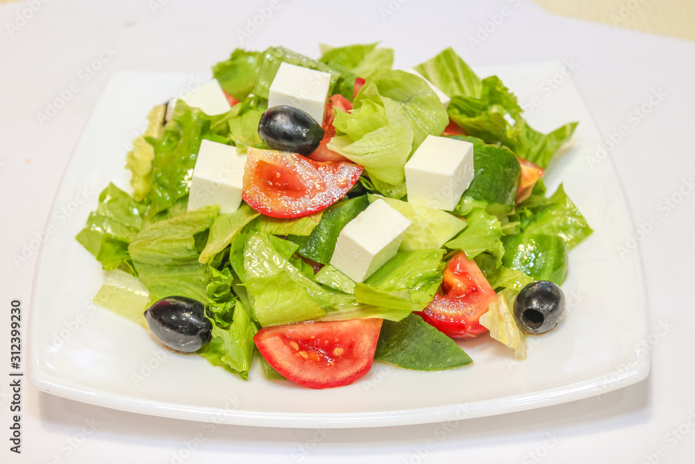 Photo of a Greek salad on a white plate with tomatoes, olives, feta cheese and herbs. Photo of a Greek salad on a white plate with tomatoes, olives, feta cheese and herbs.