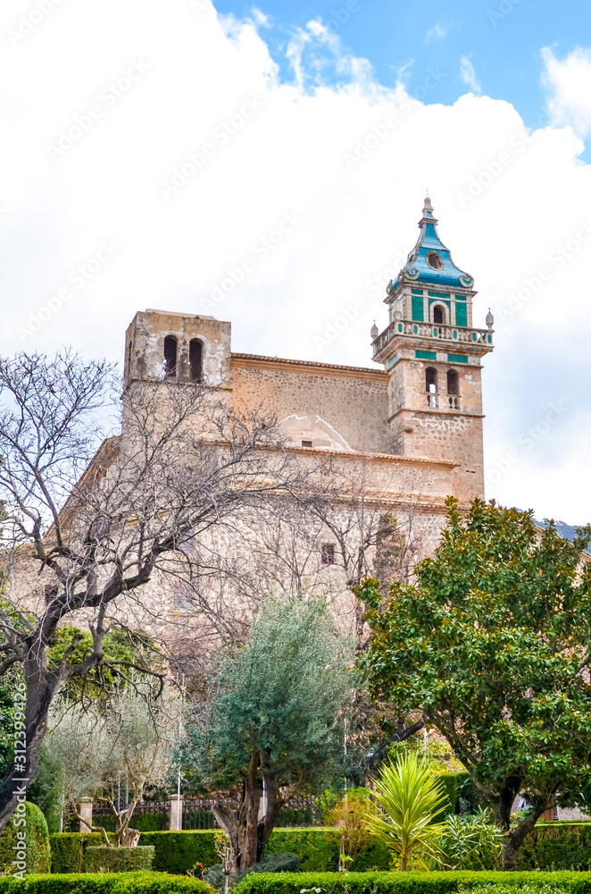 The building of the Carthusian Monastery of Valldemossa, in Valldemossa, Mallorca, Spain surrounded by green trees in the courtyard. Famous Charterhouse of Valldemossa, Spanish tourist attraction