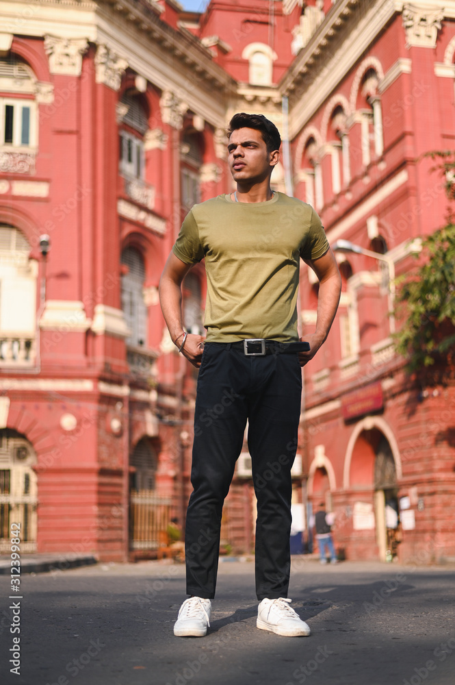  Attractive young man wearing a green t-shirt and black jeans standing on a road near old heritage building , Men's fashion 