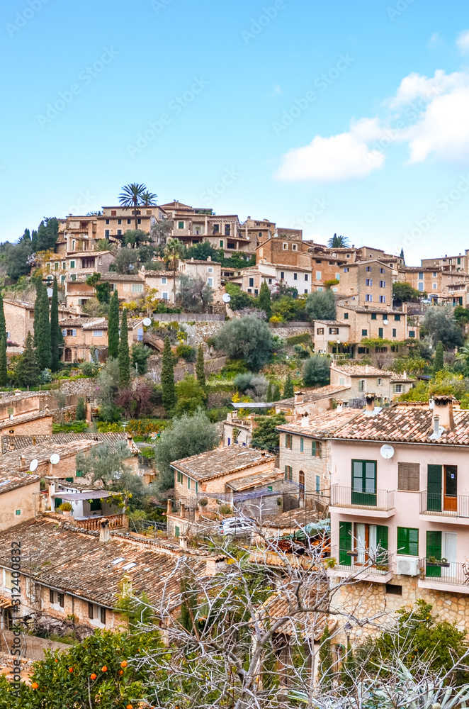 Amazing cityscape of the small coastal village Deia in Mallorca, Spain. Typical houses located in terraces on the hill surrounded by green trees. Spanish tourist attraction. Vertical photo