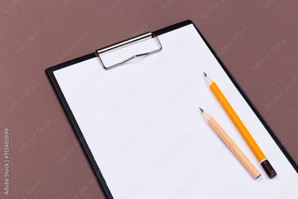 Clipboard with a white sheet and pen on a gray-dark background. View from above. space for text Clipboard with a white sheet and pen on a gray-dark background. View from above. space for text