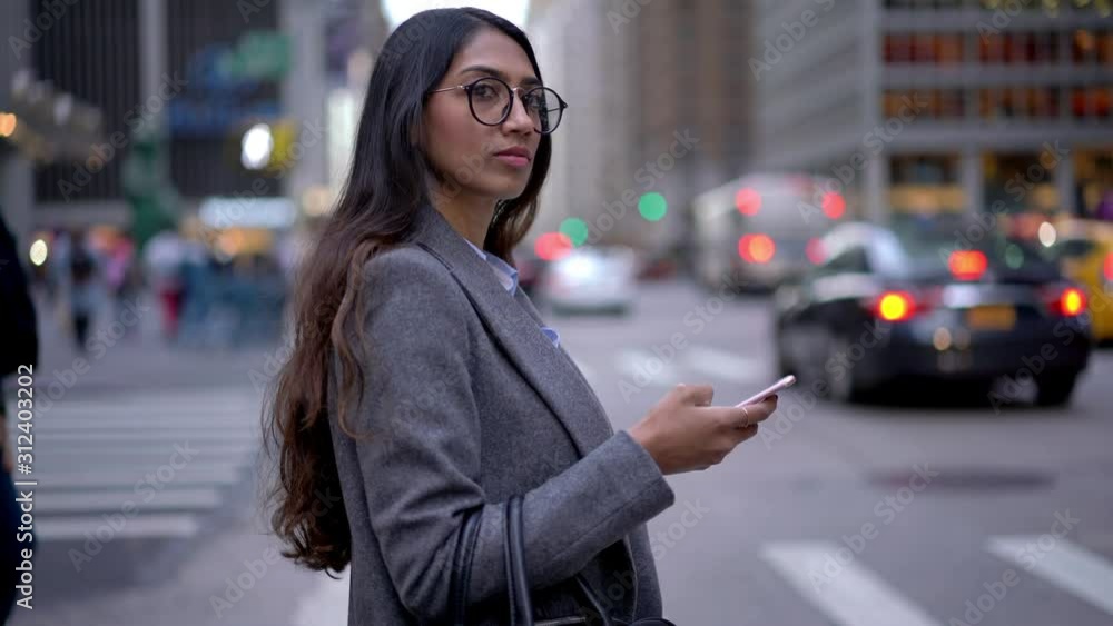 Young entrepreneur in classic spectacles and formal clothing standing near transportation road and waiting for metropolitan crosswalk in financial district holding cellphone device and looking around Young entrepreneur in classic spectacles and formal clothing standing near transportation road and waiting for metropolitan crosswalk in financial district holding cellphone device and looking around