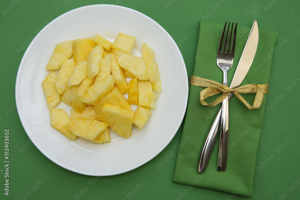 pineapple slices on a white plate on a green background with cutlery, fork and knife on a green cloth napkin. Flat lay. Top view. Restaurant menu. Vegetarian diet pineapple slices on a white plate on a green background with cutlery, fork and knife on a green cloth napkin. Flat lay. Top view. Restaurant menu. Vegetarian diet