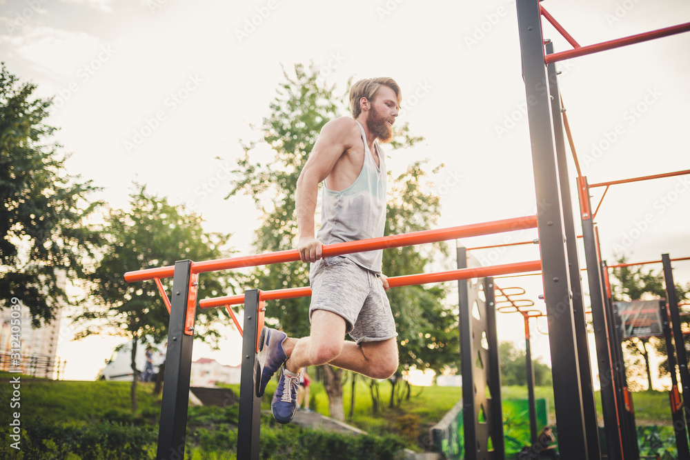 Fit Man Workout Out Arms On Dips Horizontal Bars Training Triceps And Biceps Doing Push Ups. Handsome Man Doing Exercise On Parallel Bars. Male Athlete Exercises On Parallel Bars Outdoor
