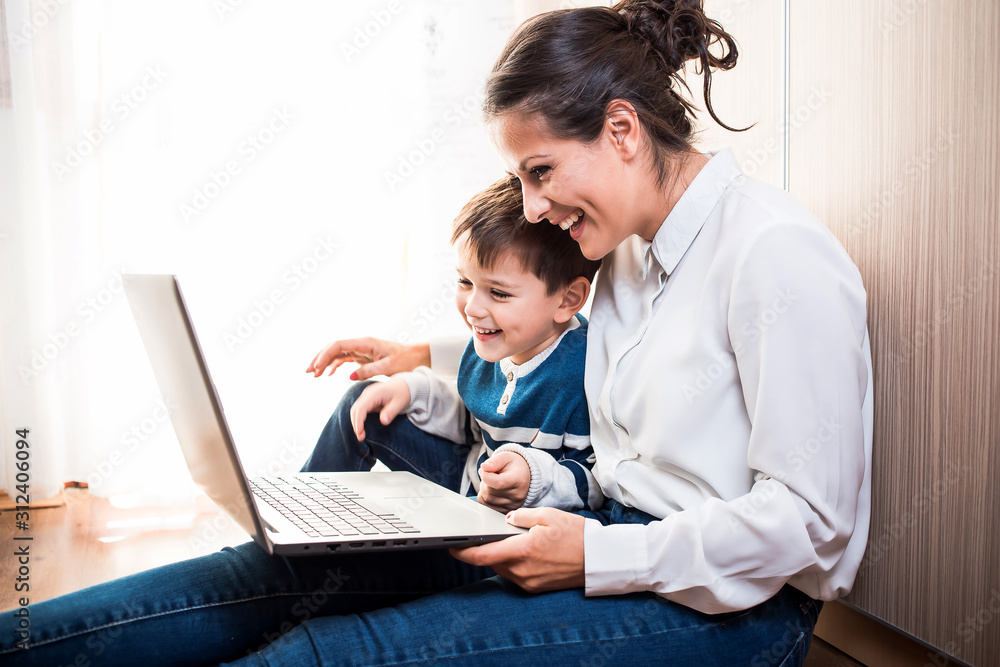 Young mom and her son, sitting on the floor looking at laptop. Video call Young mom and her son, sitting on the floor looking at laptop. Video call