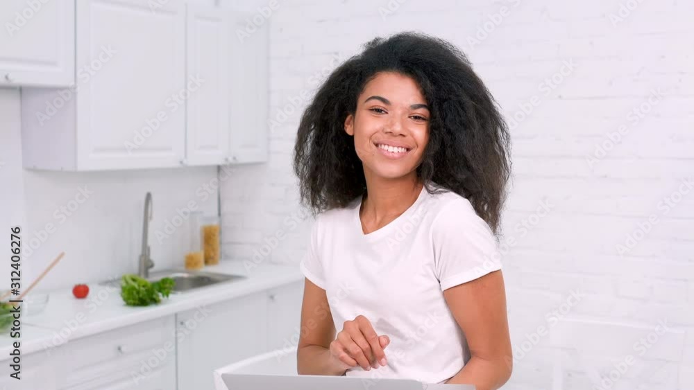 Portrait of happy and smiling afro american woman in the kitchen. Holding laptop and looking at the camera. Portrait of happy and smiling afro american woman in the kitchen. Holding laptop and looking at the camera.