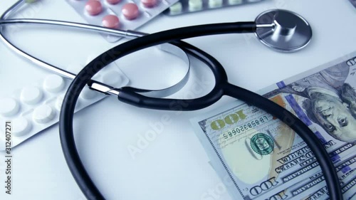 A stethoscope lies on a bundle of money and pills on  a white background. The concept of expensive medicine, medical insurance, expensive drugs.