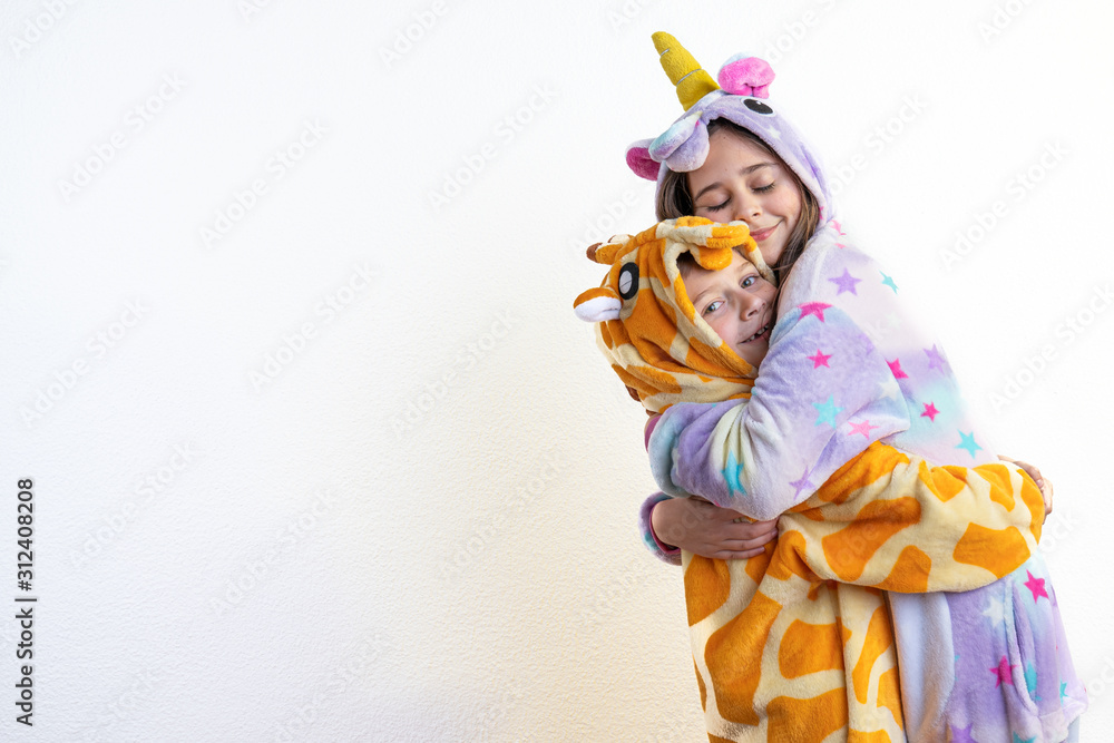 Naklejka premium Cute children, boy and girl, brother in giraffe pajamas and sister in unicorn pajamas hug each other, isolated over white background, lovely family concept