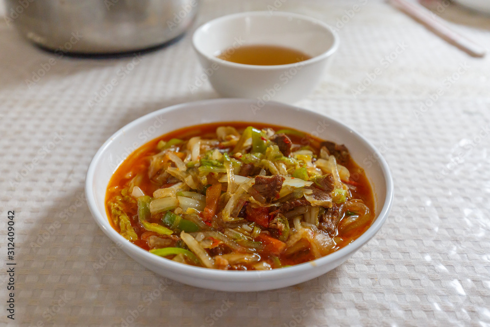 TURPAN, XINJIANG / CHINA - October 6, 2017: White plate with Laghman noodles. Ingredients include vegetables like celery, red and green pepper and lamb meat. In the back a cup of tea. Xinjiang food. TURPAN, XINJIANG / CHINA - October 6, 2017: White plate with Laghman noodles. Ingredients include vegetables like celery, red and green pepper and lamb meat. In the back a cup of tea. Xinjiang food.