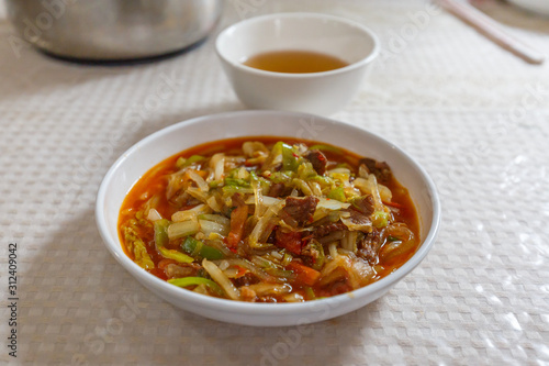 TURPAN, XINJIANG / CHINA - October 6, 2017: White plate with Laghman noodles. Ingredients include vegetables like celery, red and green pepper and lamb meat. In the back a cup of tea. Xinjiang food.