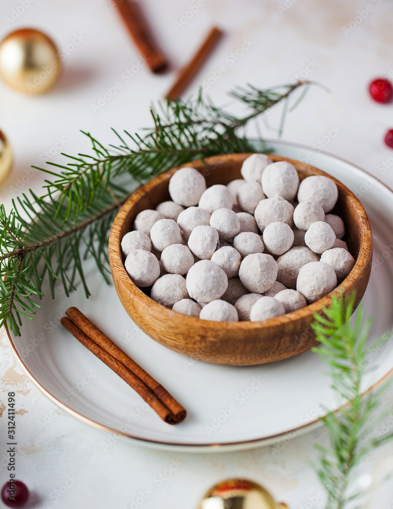 A handful of cranberries in powdered sugar on a wooden plate, next to cinnamon sticks, fresh cranberries, spruce branches and Christmas balls.