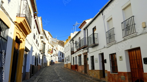 malerische enge Straße durch Ronda in Andalusien mit weißen Häusern unter blauem Himmel