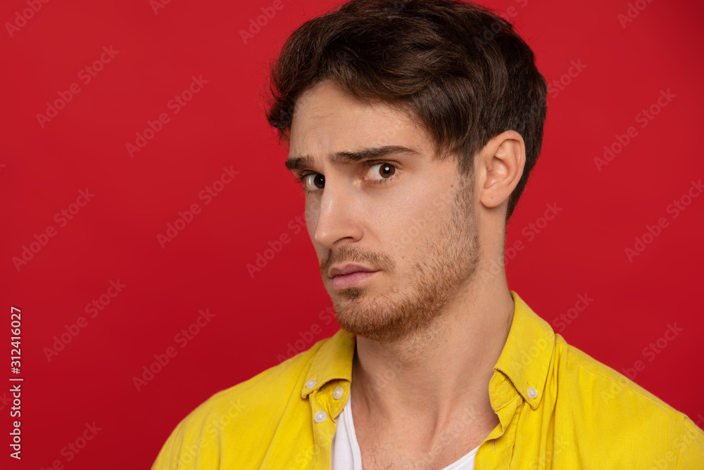 worried man in yellow shirt looking at camera isolated on red background. Face expressions concept worried man in yellow shirt looking at camera isolated on red background. Face expressions concept