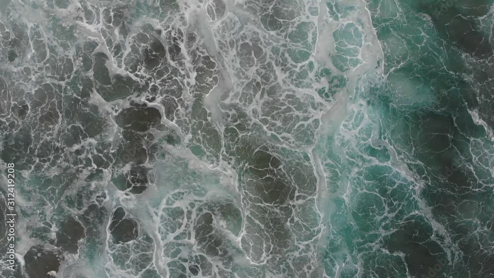 An aerial view of the wild and roaring Atlantic. The view is directed vertically downwards. A big wave rolls under the drone towards the beach. The air is full of haze. An aerial view of the wild and roaring Atlantic. The view is directed vertically downwards. A big wave rolls under the drone towards the beach. The air is full of haze.