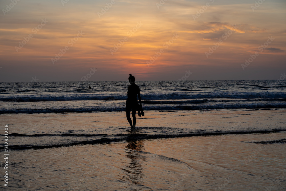 Φωτογραφία Silhouette of a girl walking on the water on a beach with her shoes in hand as t