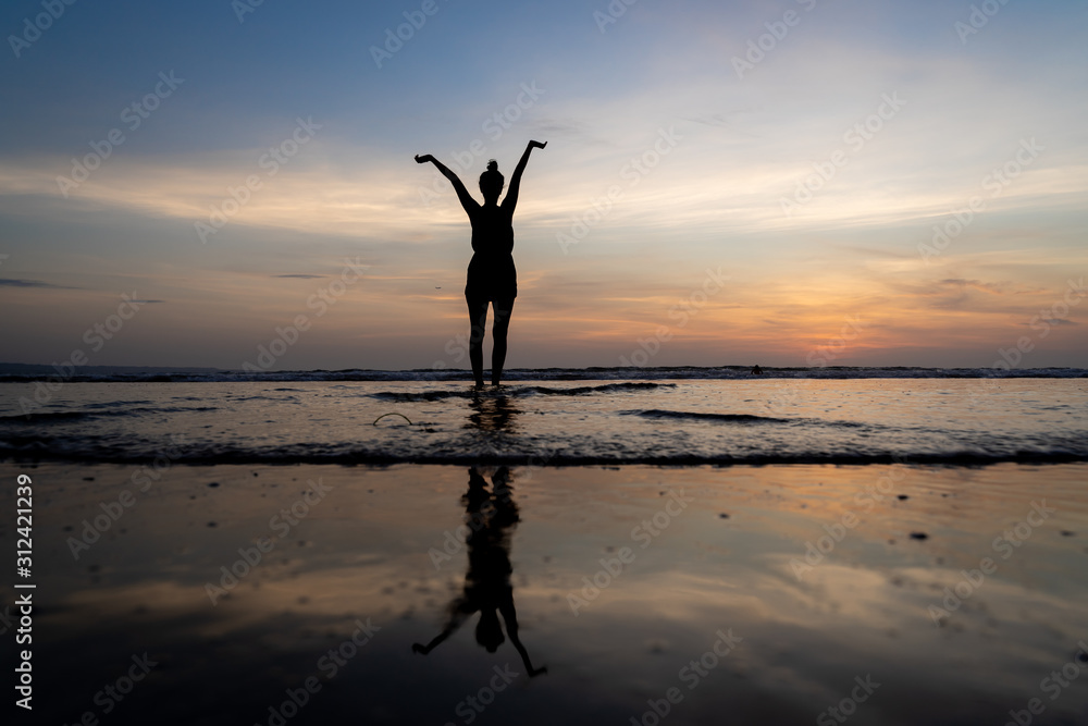 Silhouette of a girl standing in the water with her arms raised and her reflection in the water