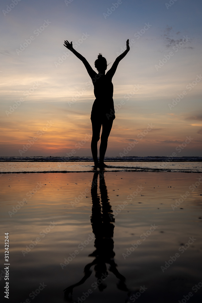 Silhouette of a girl standing in the water with her arms raised