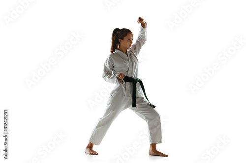 Confident junior in kimono practicing hand-to-hand combat, martial arts. Young female mongol fighter with green belt training on white studio background. Concept of healthy lifestyle, sport, action.