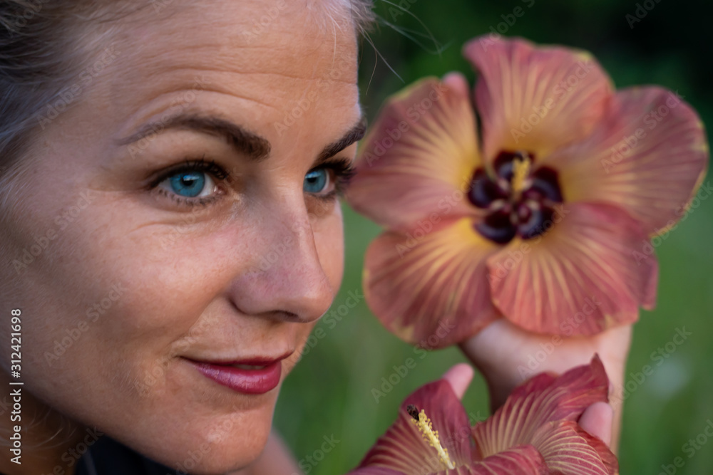Blonde young woman with blue eyes showing some flowers next to her face Blonde young woman with blue eyes showing some flowers next to her face