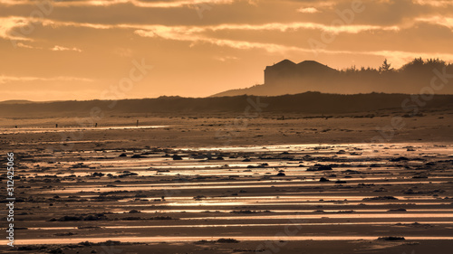 Golden winter evening light on Brora beach with golden lines of water left by the receding tide reflecting the light of the sunset. photo