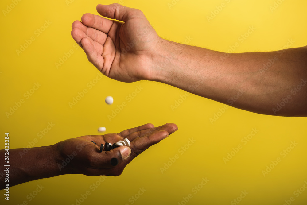 Fototapeta premium two male hands one black male second European man holding and flipping pills white and black