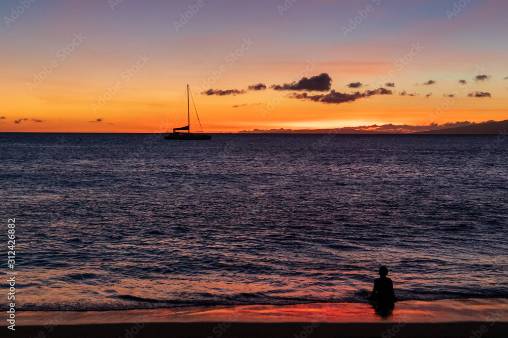 Little boy sitting in the warm Hawaiian ocean, watching the beatiful sunset.