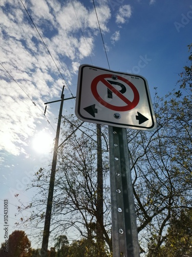No Parking sign with left and right arrows before hydro line and sun.