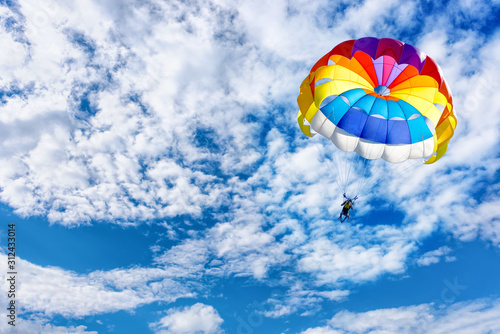 A man is gliding using a parachute on the background of cloudy blue sky.