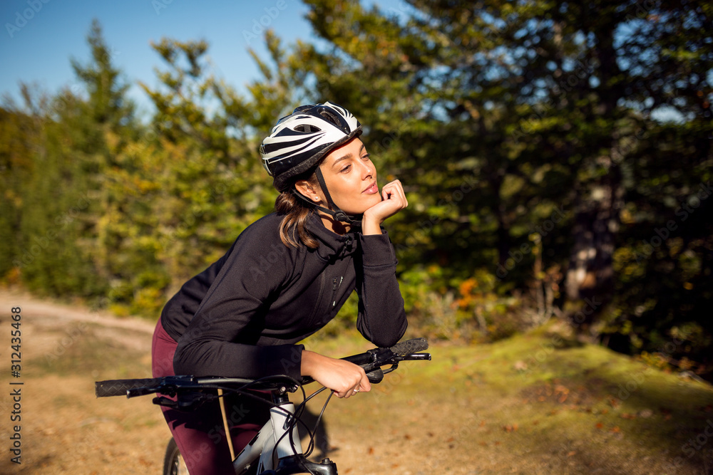 Fototapeta premium Cute young female cyclist with bike in nature environment