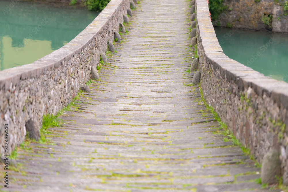 Obraz premium Bridge of a devil. Bridge over the river in Tuscany. Built in the 11 century. Ancient masonry covered with moss.