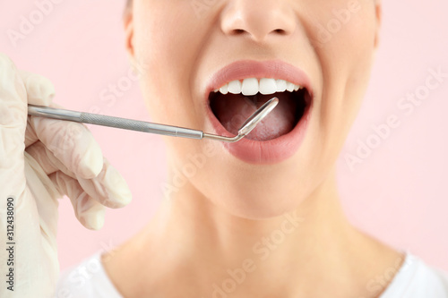 Dentist examining teeth of beautiful young woman against color background