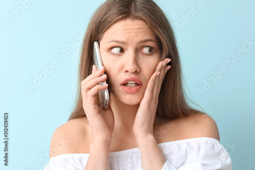 Afraid woman talking by mobile phone on color background
