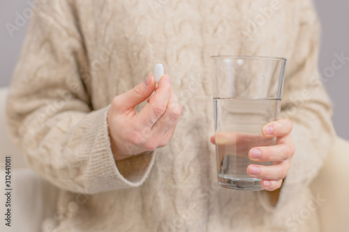 Woman is holding pill and glass of water in her hand photo