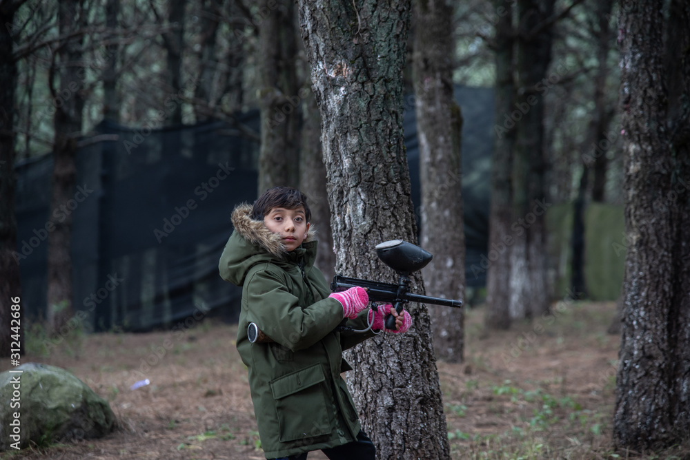 boy with green jacket playing gotcha in the woods among trees