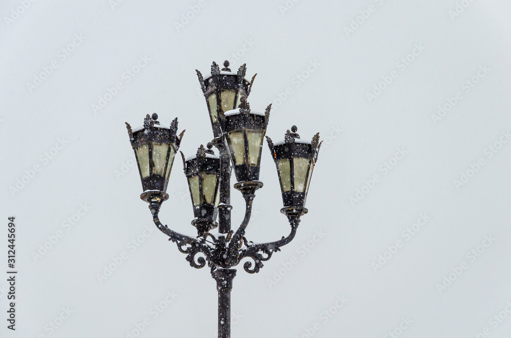 Lights and lanterns on a pole on a winter day under snow.