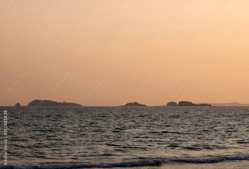 Tropical islands with a bright orange sunset sky and sunlight reflecting on the ocean for a summer holiday background concept.