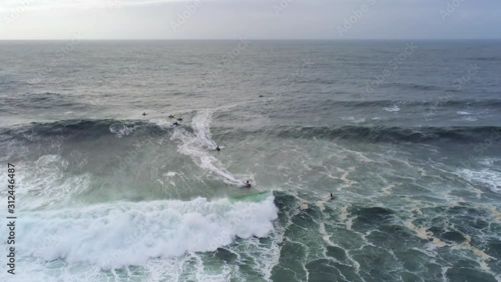 Aerial: bird's eye view of unrecognisable surfers catching a giant wave in popular surfing destination. Nazare, Portugal. Aerial: bird's eye view of unrecognisable surfers catching a giant wave in popular surfing destination. Nazare, Portugal.