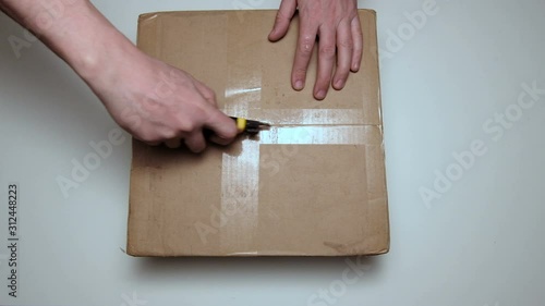 Unpacking the parcel. Male hand close up. Cardboard box with a surprise. A man cuts the packaging with a knife.