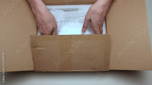 Unpacking the parcel. A man from a package takes out something white from metal. Male hand close up. Cardboard box with a surprise.