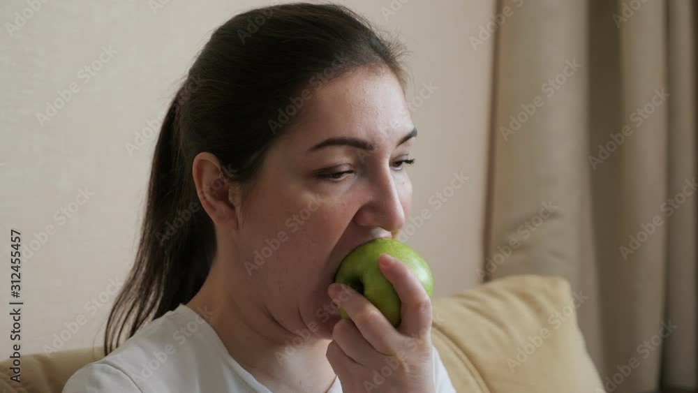 plump woman is eating an apple while sitting on the sofa, close-up plump woman is eating an apple while sitting on the sofa, close-up