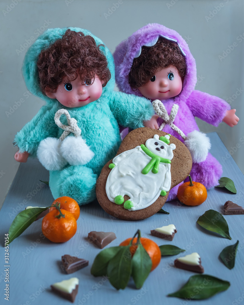 Greeting card with twin dolls in bright costumes with glazed gingerbread and tangerines Greeting card with twin dolls in bright costumes with glazed gingerbread and tangerines