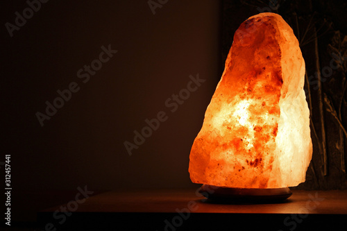 Himalayan salt lamp on wooden table illuminated in a darkend room