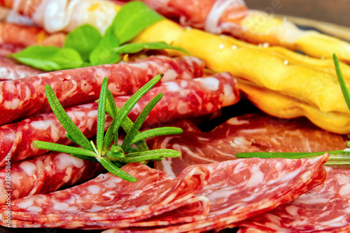 Beautiful sliced food arrangement close-up photo. Italian style antipasto plate, cheese, ham, salami, rosmarin, prosciutto