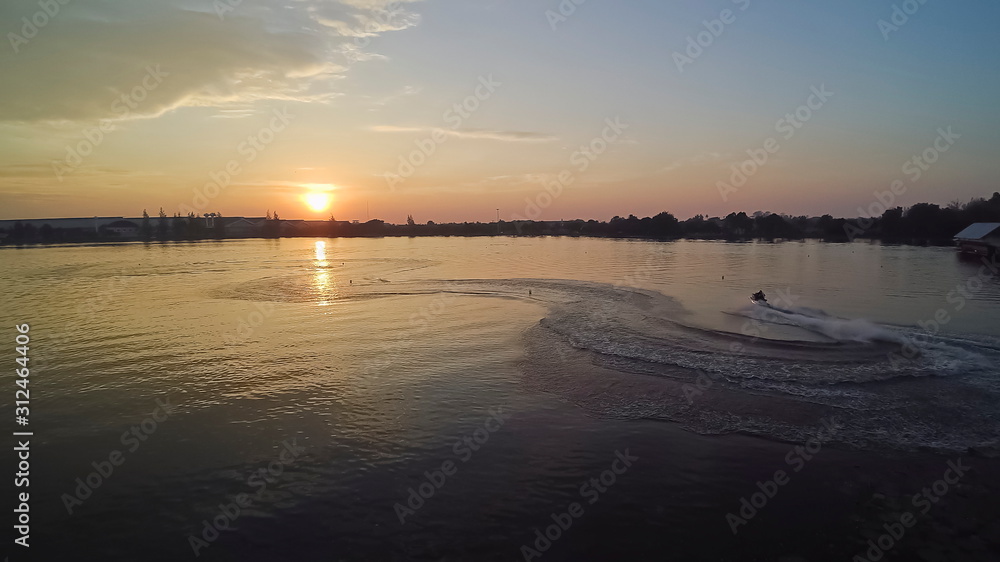 Aerial view evening above the lake, view of jet ski running in the lake with yellow sunshine and blue sky background, sunset at Krajub reservoir, Ban Pong District, Ratchaburi, Thailand.