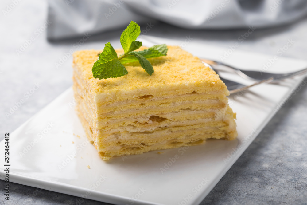 Piece of cake Napoleon on white plate on concrete background, close up view. Traditional millefeuille dessert with puff pastry and custard, copy space. Piece of cake Napoleon on white plate on concrete background, close up view. Traditional millefeuille dessert with puff pastry and custard, copy space.