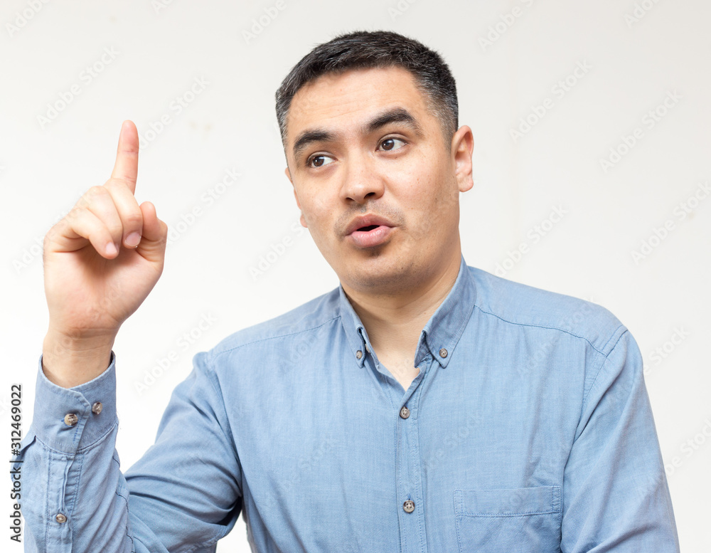 Portrait of a man in a blue shirt shows his index finger upwards on a white background Portrait of a man in a blue shirt shows his index finger upwards on a white background