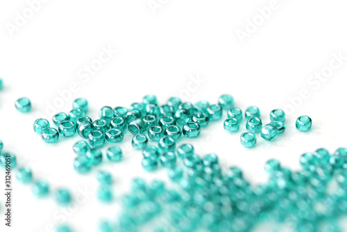 Transparent seed beads aquamarine color scattered on a white surface close-up