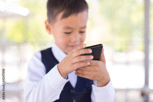 A boy in a school uniform holds a smartphone, talking loudly