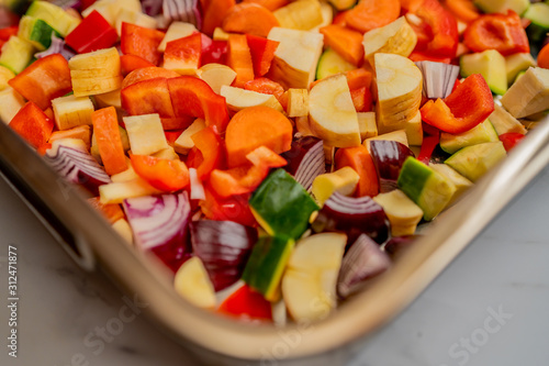  Close up and selective focus of Mediterranean vegetables in a stainless steel baking tray on a white marbled background