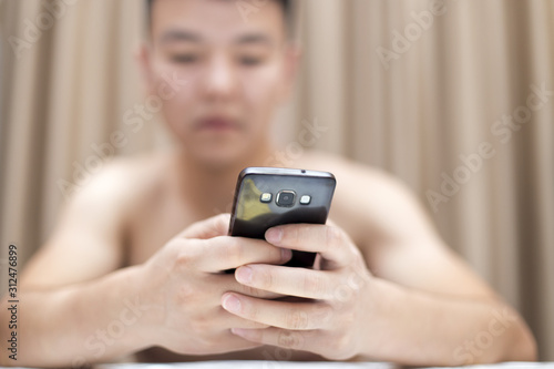 Handsome casual young man sitting at home, reading a sms on his mobile phone with a smile